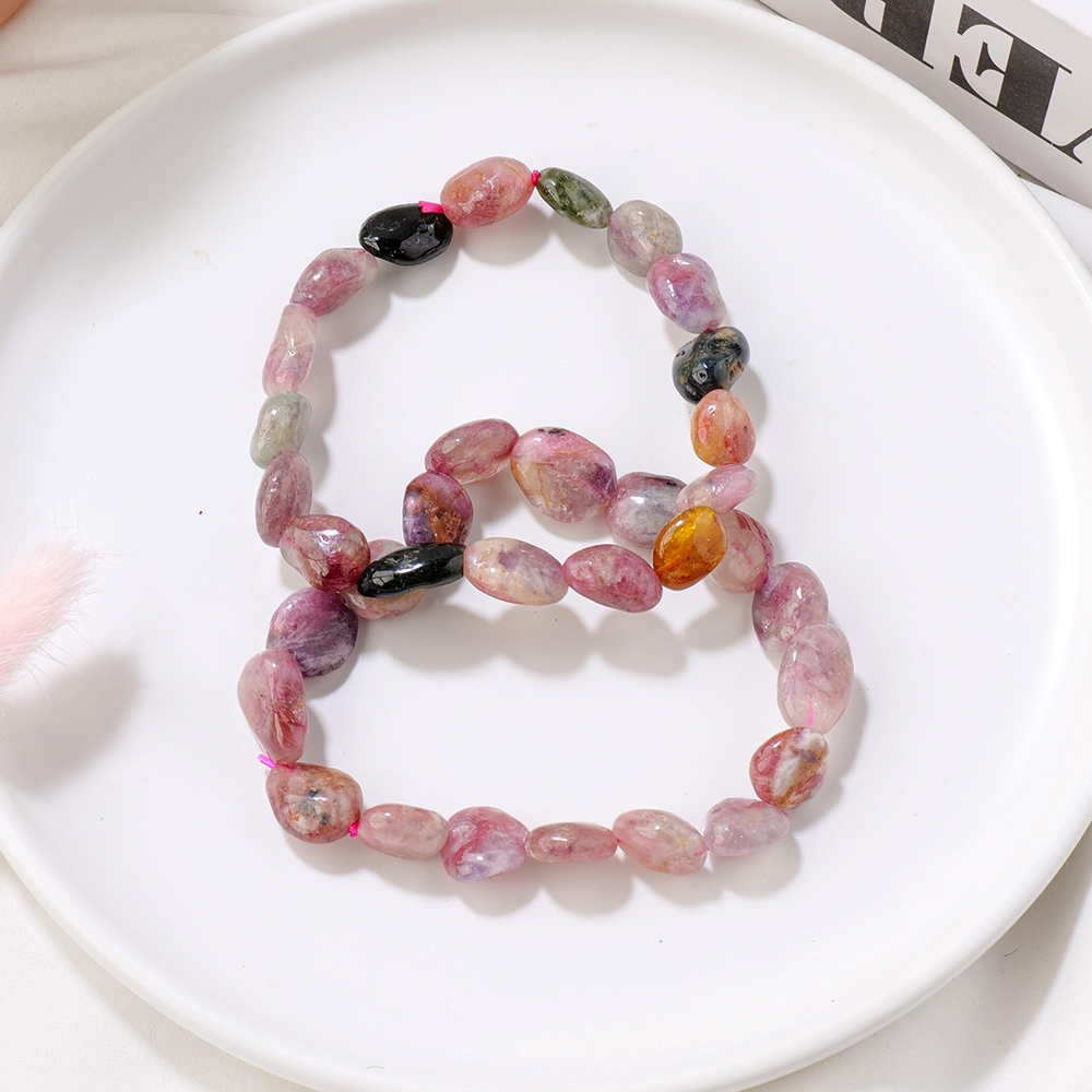 Deux bracelets de tourmaline posés dans une assiette blanche. À côté de l'assiette, l'on aperçoit un livre posé.