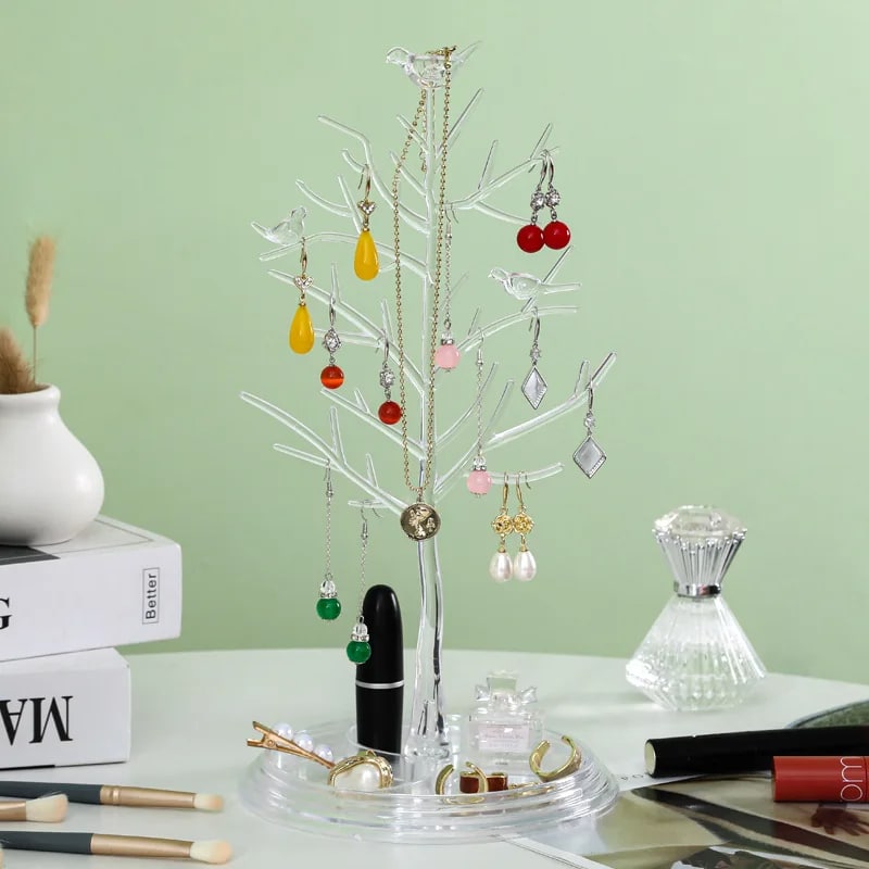 Arbre à Bijoux Pratique et Transparent avec Oiseaux posé sur une table avec des objets sur fond vert