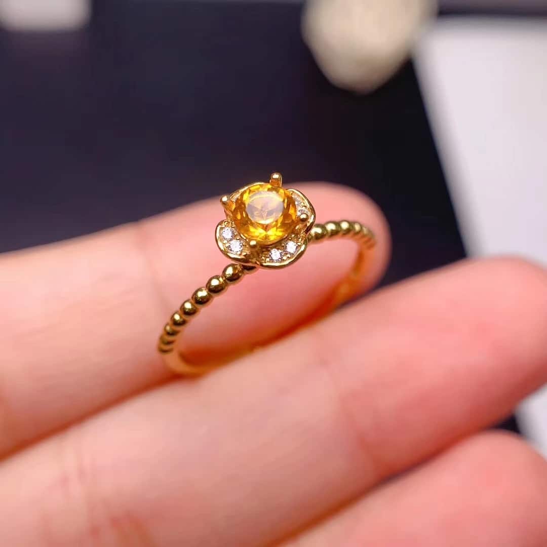 Bague Citrine au Design de Fleur en Argent tenue entre deux doigts