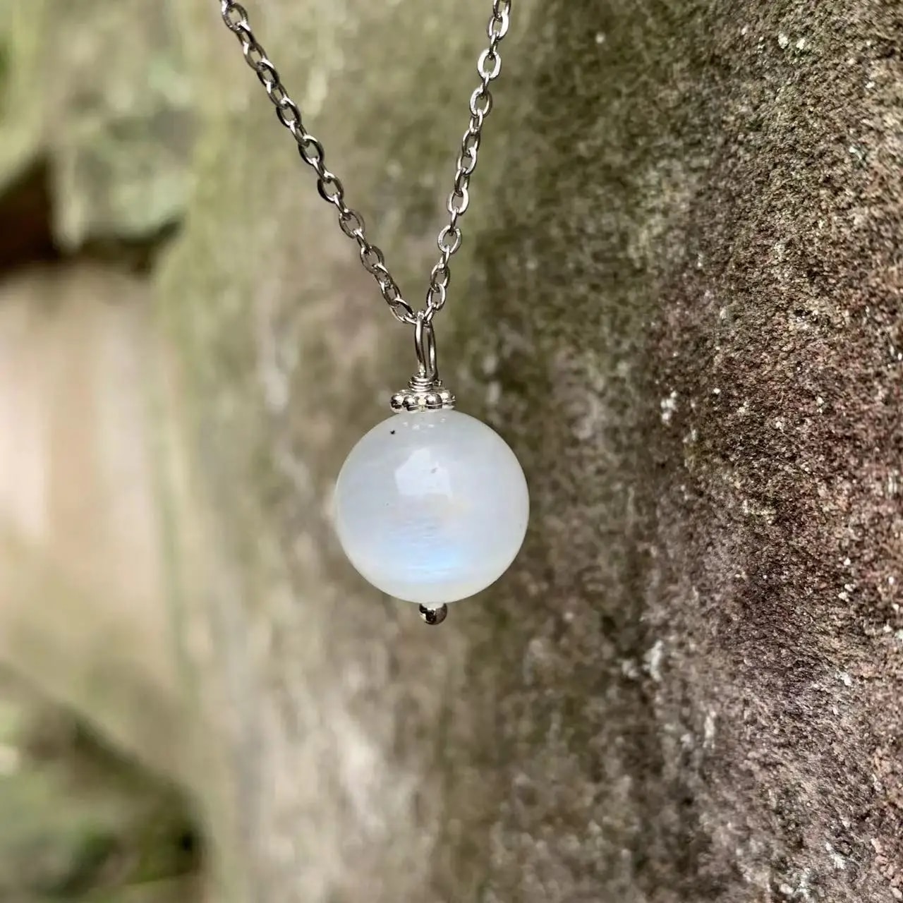 Pendentif Pierre de Lune avec Chaine en Acier Inoxydable devant un mur en extérieur