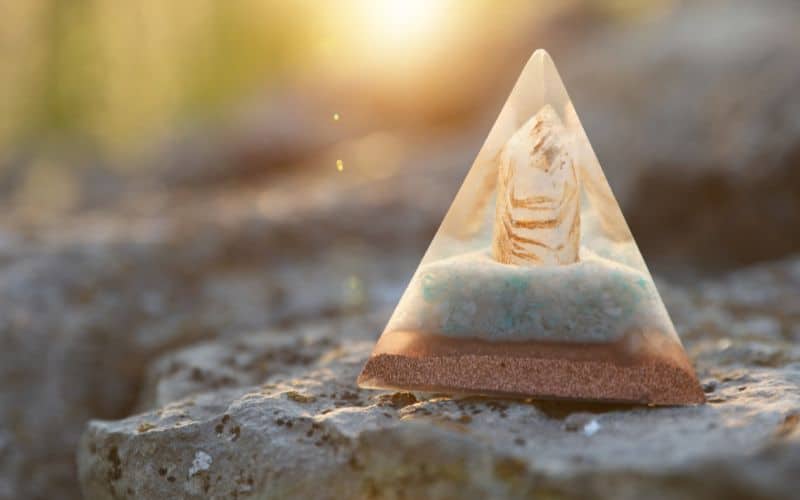 Pyramide orgonite posé sur un rocher avec le soleil flou en fond.