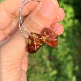 Boucles d'Oreilles Ambre Rondes dans les mains d'une personne sur fond vert
